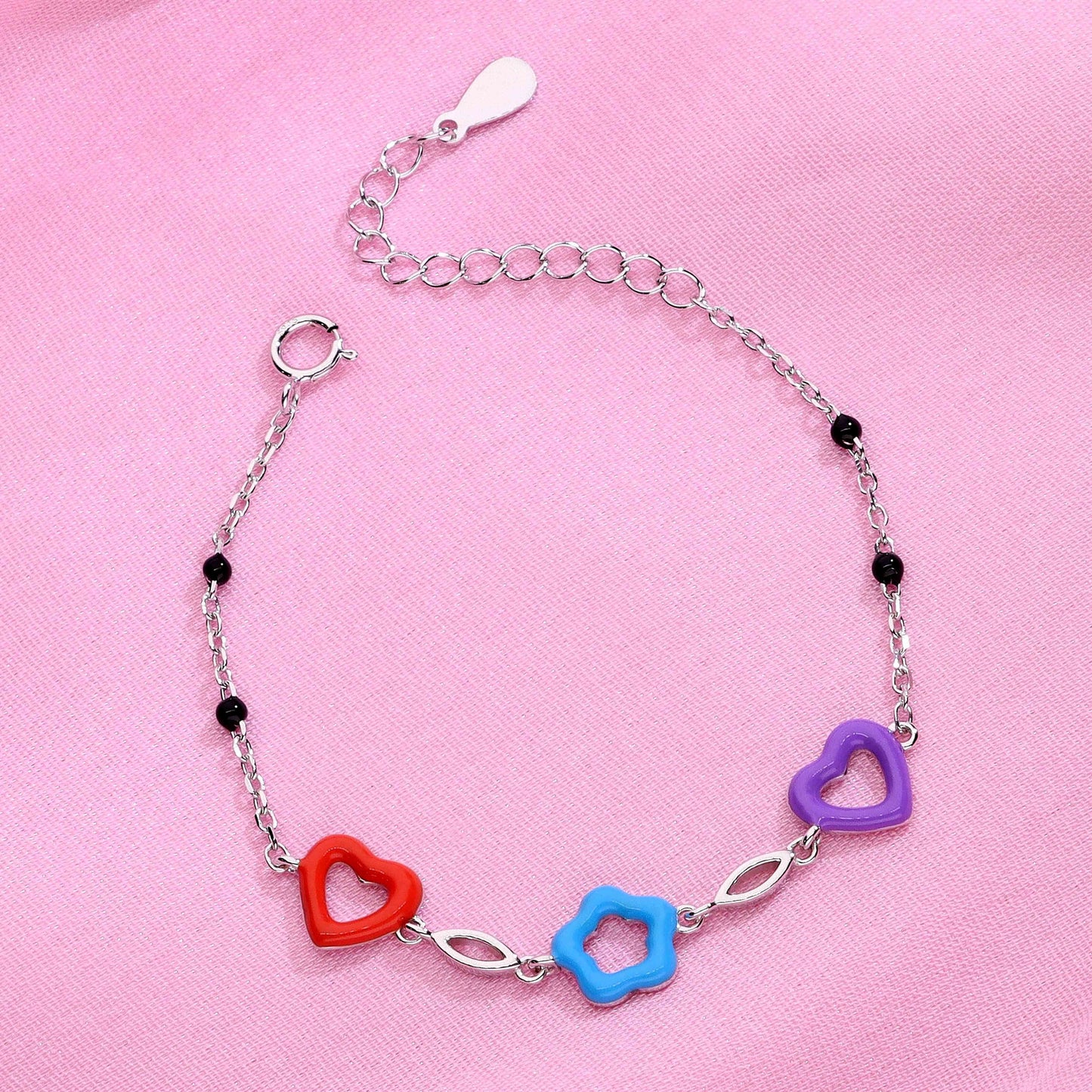 Children’s charm bracelet with red and purple heart shapes, blue flower charm, and silver chain