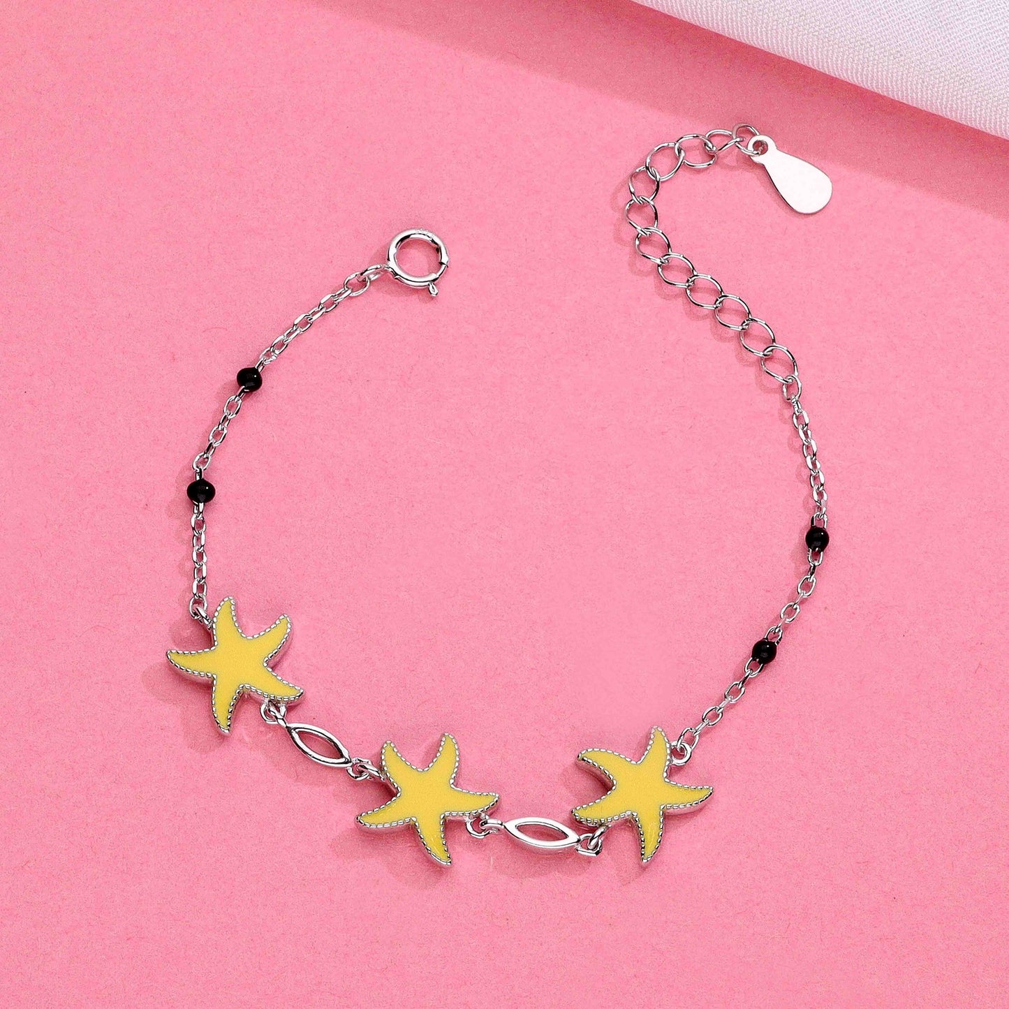 Silver chain bracelet with three yellow starfish charms, black bead accents