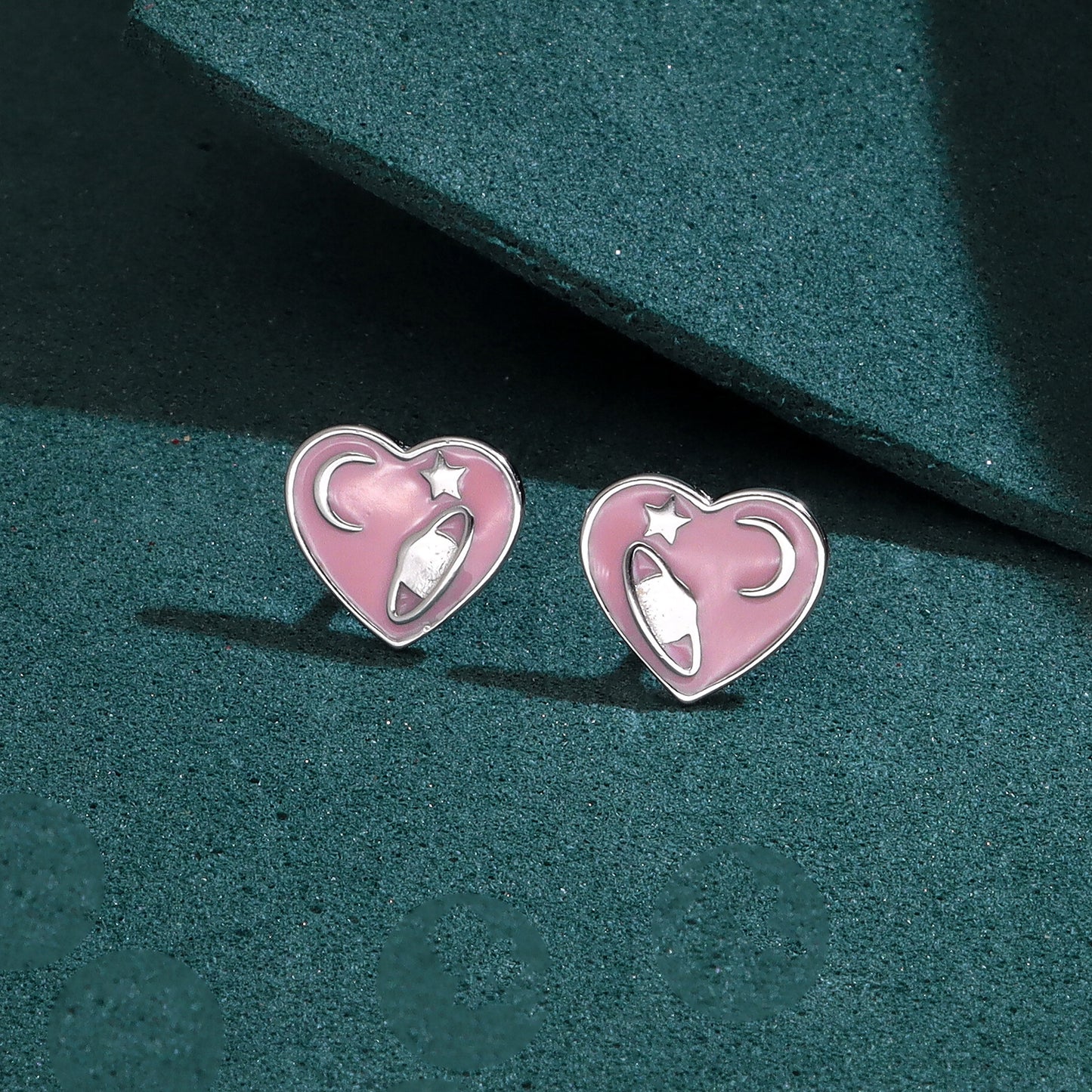 Pair of sterling silver pink heart stud earrings with a space-themed design featuring a rocket, moon, and star